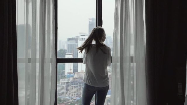 Attractive young woman alone with her thoughts standing by the window at home.