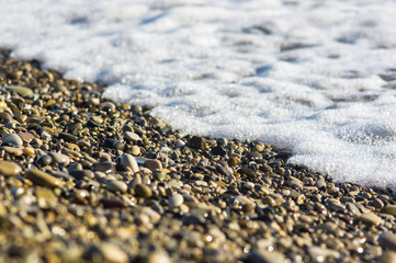 pebble stones on the sea beach, the rolling waves of the sea with foam