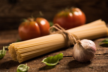 Spaghetti and tomatoes with herbs on an old and vintage wooden table. Pasta ingredients