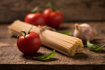 Spaghetti and tomatoes with herbs on an old and vintage wooden table. Pasta ingredients