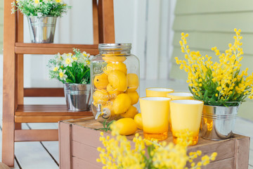 The glass jar is completely filled with lemons and beside it there are yellow glasses on a wooden...