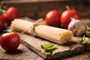 Spaghetti and tomatoes with herbs on an old and vintage wooden table. Pasta ingredients