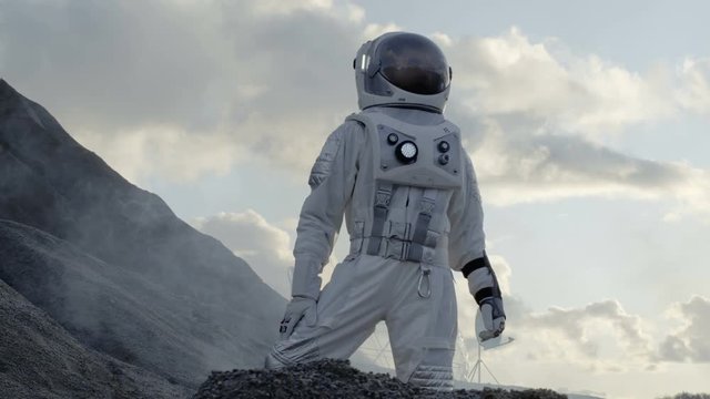 Astronaut Looking Around while Standing on the Hill of the Frozen Alien Planet. In the Background His Base/ Research Station. Shot on RED EPIC-W 8K Helium Cinema Camera.