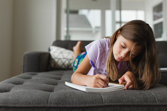 Preteen girl writing in a journal while laying on sofa at home