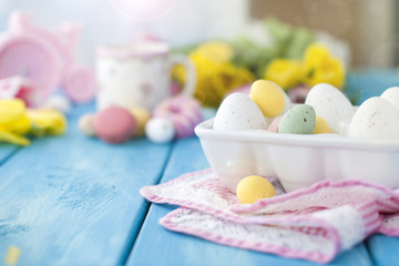 Cells with Easter eggs of different colors. Blue wood background. A pink napkin. Free space for text