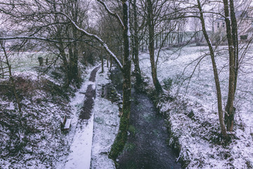 Rural setting in the village of Carrignavar during Storm Emma, also known as the Beast from the East, which hit Ireland at the start of March: stream surrounded by trees and roads covered in snow.