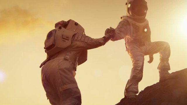 Two Astronauts Climbing Mountain Hill Helping Each Other, Reaching the Top. Helping Hand. Overcoming Difficulties.