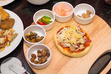 Prepare homemade mini pizza buns to bake and fresh ingredients on cutting board.