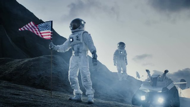 Two Proud Astronauts Plant American Flag on the Alien Planet. In the Background Research Base and Rover. Shot on RED EPIC-W 8K Helium Cinema Camera.