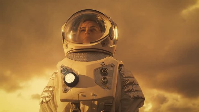 Low Angle Shot of Female Astronaut in the Space Suit Looking Around Alien Planet. Red and Orange Planet Similar to Mars. Shot on RED EPIC-W 8K Helium Cinema Camera.