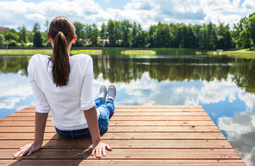 Young woman relaxing on a wooden dock by a beautiful lake. Outdoor getaways concept.