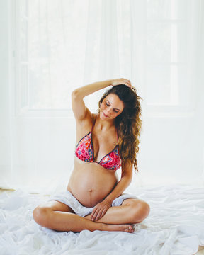 Pregnant woman in bikini sits with crossed legs and revives her long hair