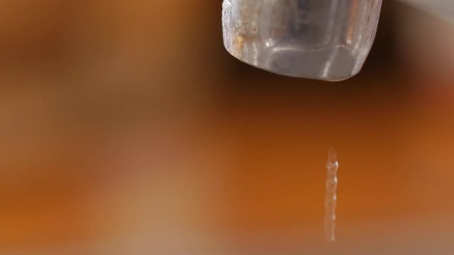 A macro of dripping kitchen faucet spout, water waste.