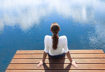 Young woman relaxing on a dock lake side. Peace and serenity concept. 