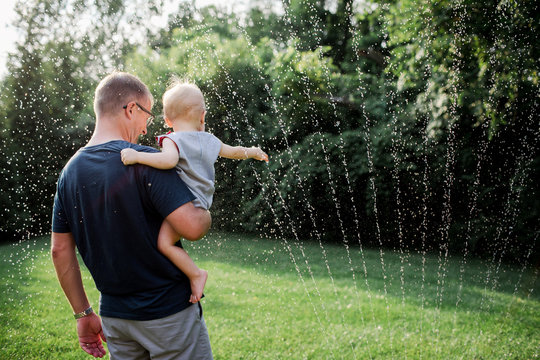 father and baby playing in a backyard sprinkler