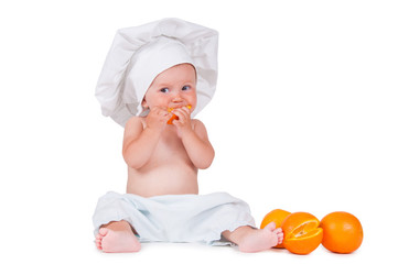 A small child eats an orange slice in a chef suit on a white background.