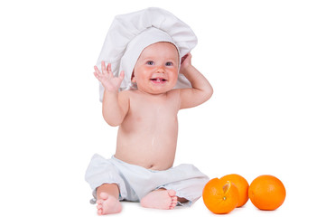 A small child eats an orange slice in a chef suit on a white background.