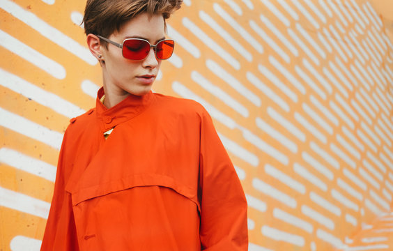 Urban stylish short hair female model in red/orange coat in front of orange background. - Powered by Adobe