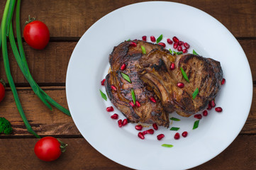 Steak on ribs, cooked on a grill with pomegranate on a white plate. Wooden rustic background. Top view