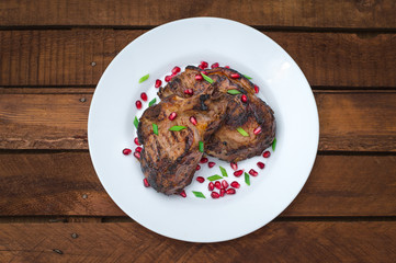 Steak on ribs, cooked on a grill with pomegranate on a white plate. Wooden rustic background. Top view