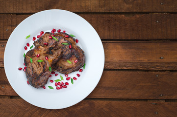 Steak on ribs, cooked on a grill with pomegranate on a white plate. Wooden rustic background. Top view