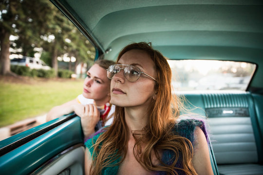 young woman looking out car window with her friend in the back seat