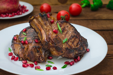 Steak on ribs, cooked on a grill with pomegranate on a white plate. Wooden rustic background. Top view