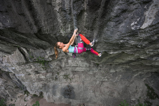 Caucasian female rock climber hanging on craggy rock wall