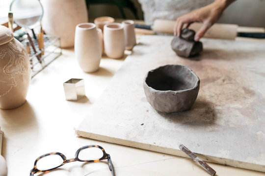 woman forming clay and creating beads and pinch pot by hand from raw materials in home studio workshop