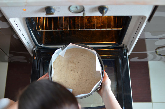 Woman hands putting biscuit cake for baking into the oven. Low DOF. Top view