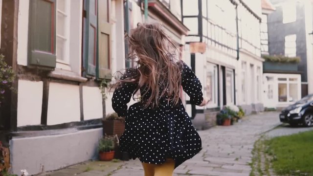 Little girl in black dress running on old road. Back view slow motion. Half-timbered houses. Happy carefree childhood.