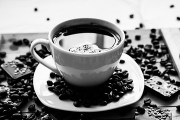 Single white cup with black coffee on wooden table with beans and almond chocolate black and white photography