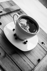 Single white cup with black coffee on wooden table with few beans black and white photography