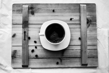 Single white cup with black coffee on wooden table with few beans black and white photography