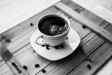 Single white cup with black coffee on wooden table with few beans black and white photography