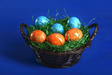 Painted Easter eggs of orange and light blue in green grass in a wicker basket.