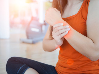Young woman massaging her wrist after working out or injured hand during careless sport practice with fitness equipment background.
