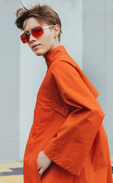 Alternative stylish young female on orange/red coat on street/minimalist composition.