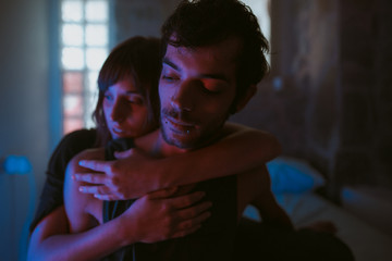 young couple hugging in a blue iluminated bedroom