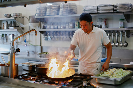 Cook in his kitchen stirring a frying pan on flames with cauliflower vegetables