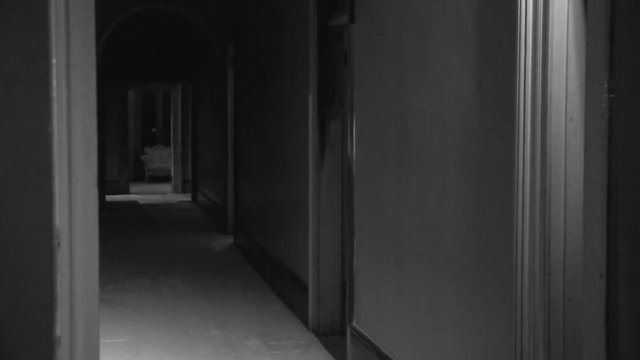 A steady black and white shot of a hallway inside a haunted house.