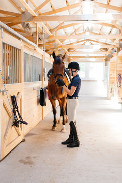 young female equestrian petting the nose of her horse in a barn