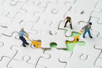 Teamwork, fulfill the missing piece for business success strategy concept, miniature workers team help using the forklift to complete the missing white jigsaw puzzle piece on pastel green background