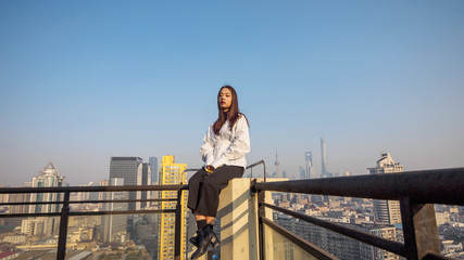 Fototapeta na wymiar Beautiful young brunette woman sit on top of mansion roof with blur Shanghai Bund landmark buildings background. Emotions, people, beauty and lifestyle concept.