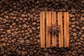Coffee grains are scattered on a wooden table with cinnamon sticks and anise star