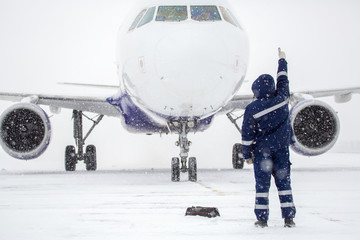 Member of ground crew park passenger airliner on airport apron in blizzard. passenger airliner taxi at airport in snow. Modern twin-engine passenger airplane taxiing at airport during snow blizzard