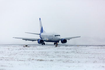 Airliner on runway in blizzard. Aircraft during taxiing at heavy snow. Passenger plane in snow at airport. Modern twin-engine passenger airplane taxiing for take off at airport during snow blizzard