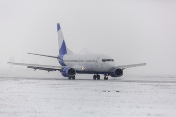 Obraz premium Airliner on runway in blizzard. Aircraft during taxiing at heavy snow. Passenger plane in snow at airport. Modern twin-engine passenger airplane taxiing for take off at airport during snow blizzard