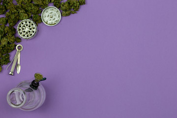 Loose medical marijuana with glass bong, metal grinder and cleaning tool on ultraviolet surface