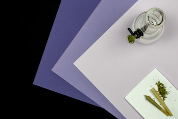 Glass bong cone shaped rolling paper with loose medical marijuana and joint on an ultraviolet...